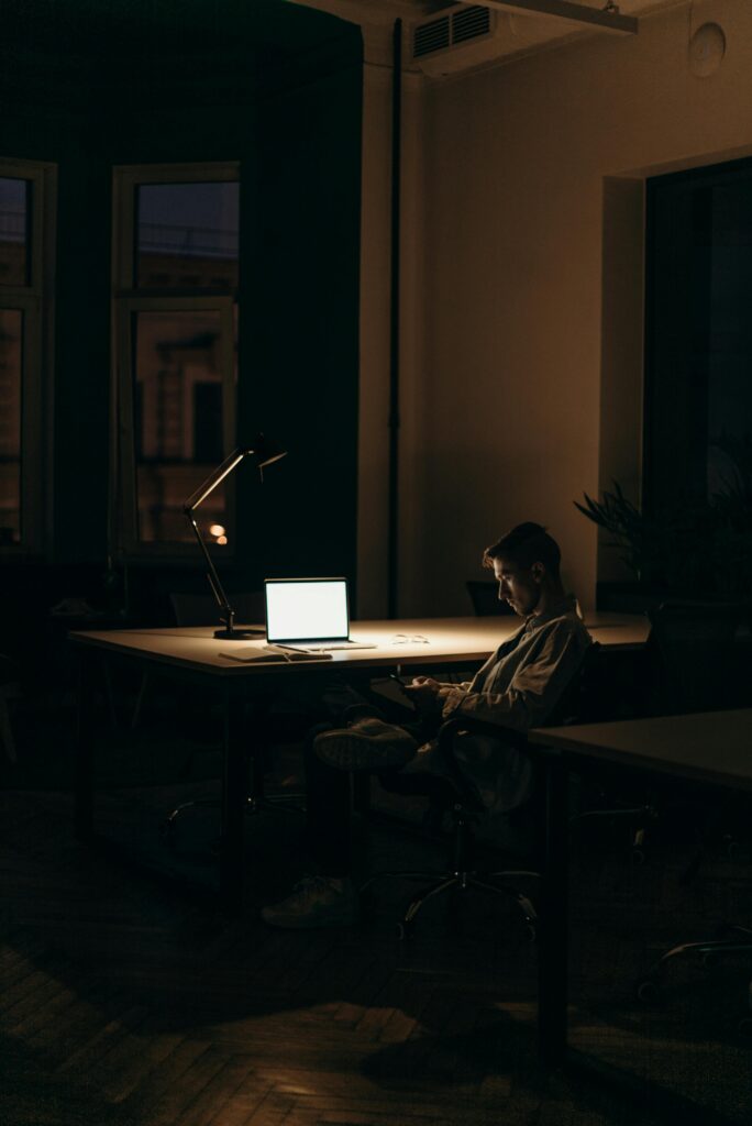 pexels-photo-4069292-4069292 A lone man working on a laptop under dim lighting in a quiet office at night.